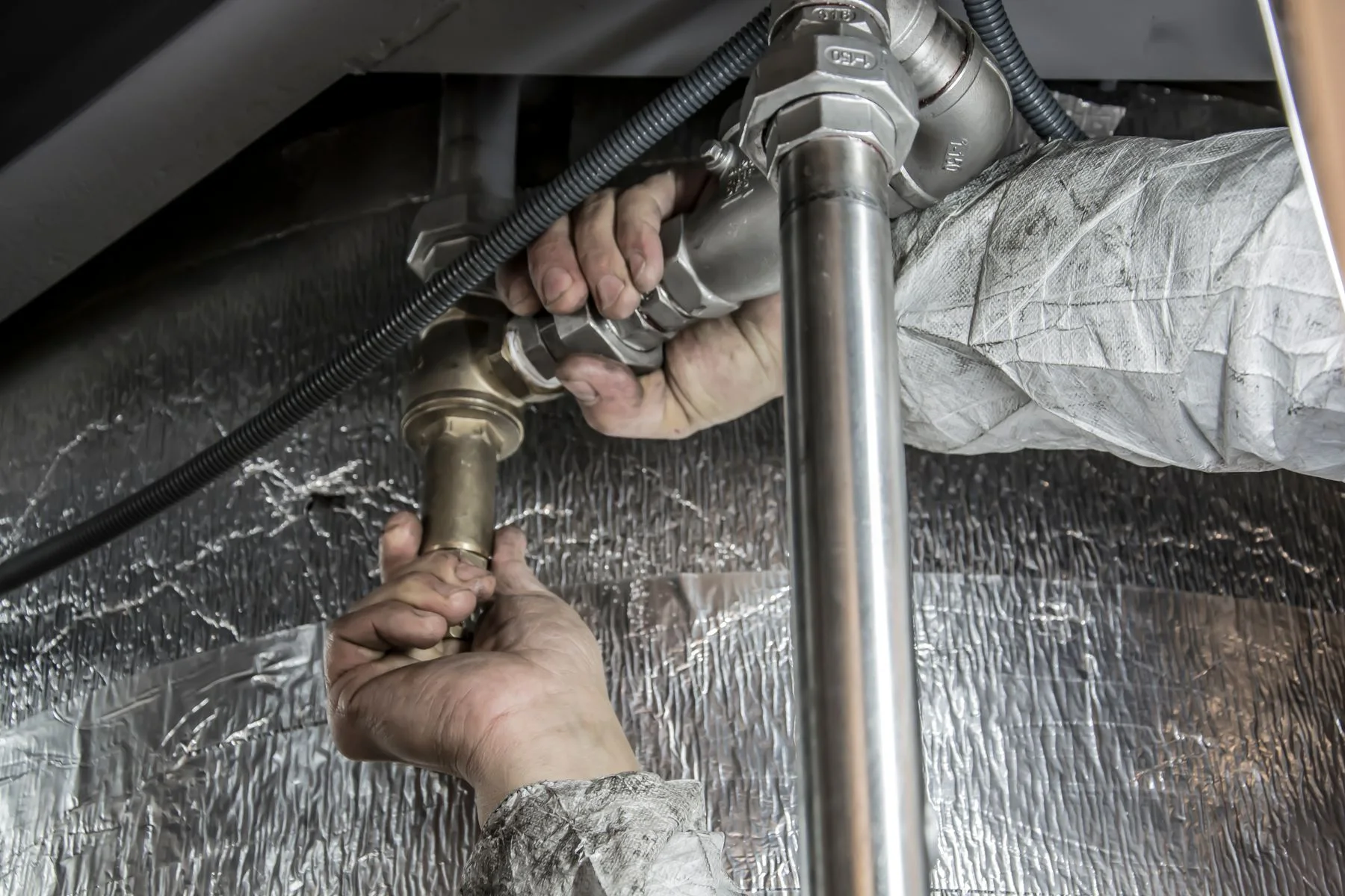A plumber fitting copper pipework beneath a kitchen sink